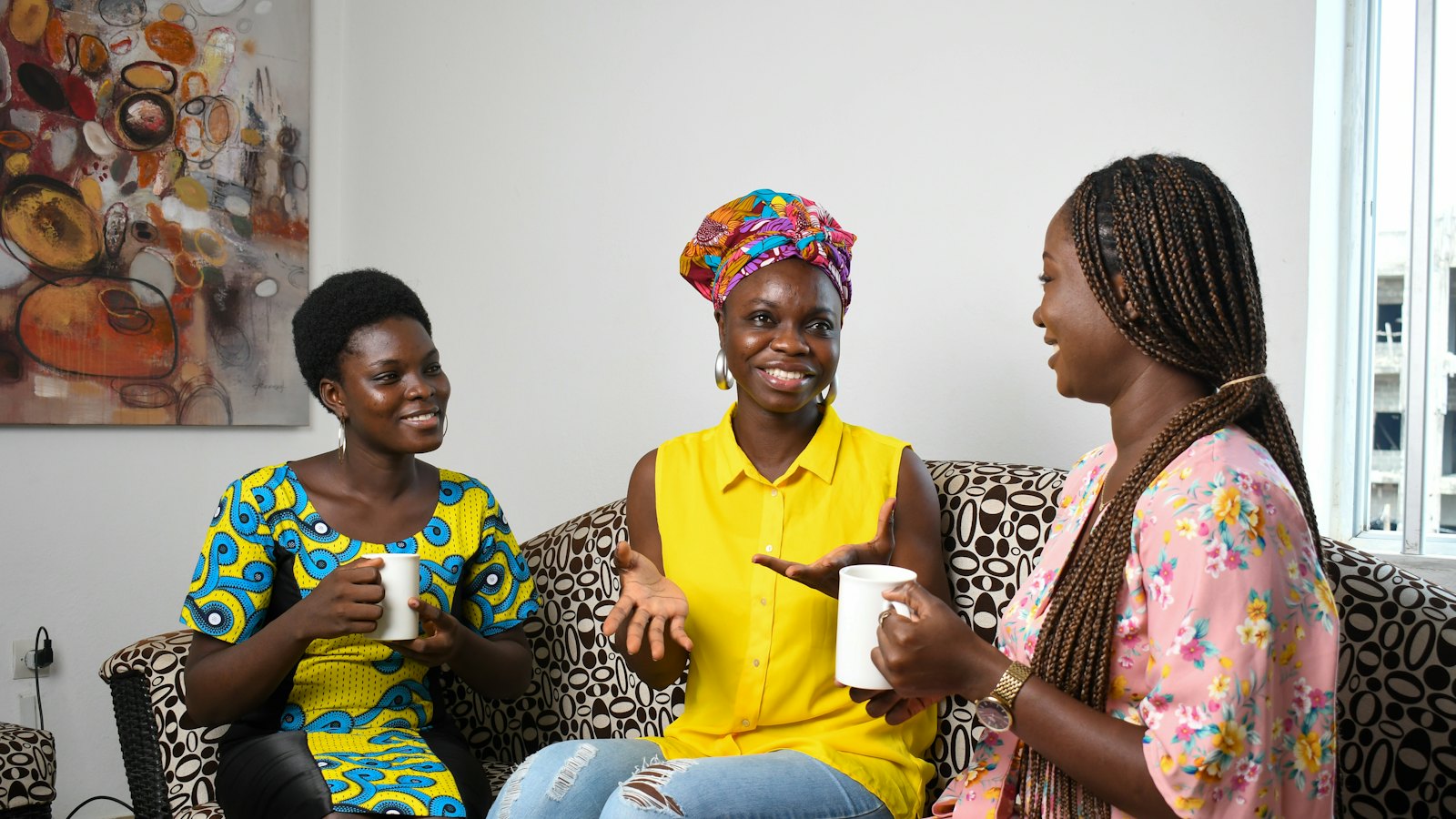 Trois jeunes femmes échangent, assises sur un canapé, un café à la main